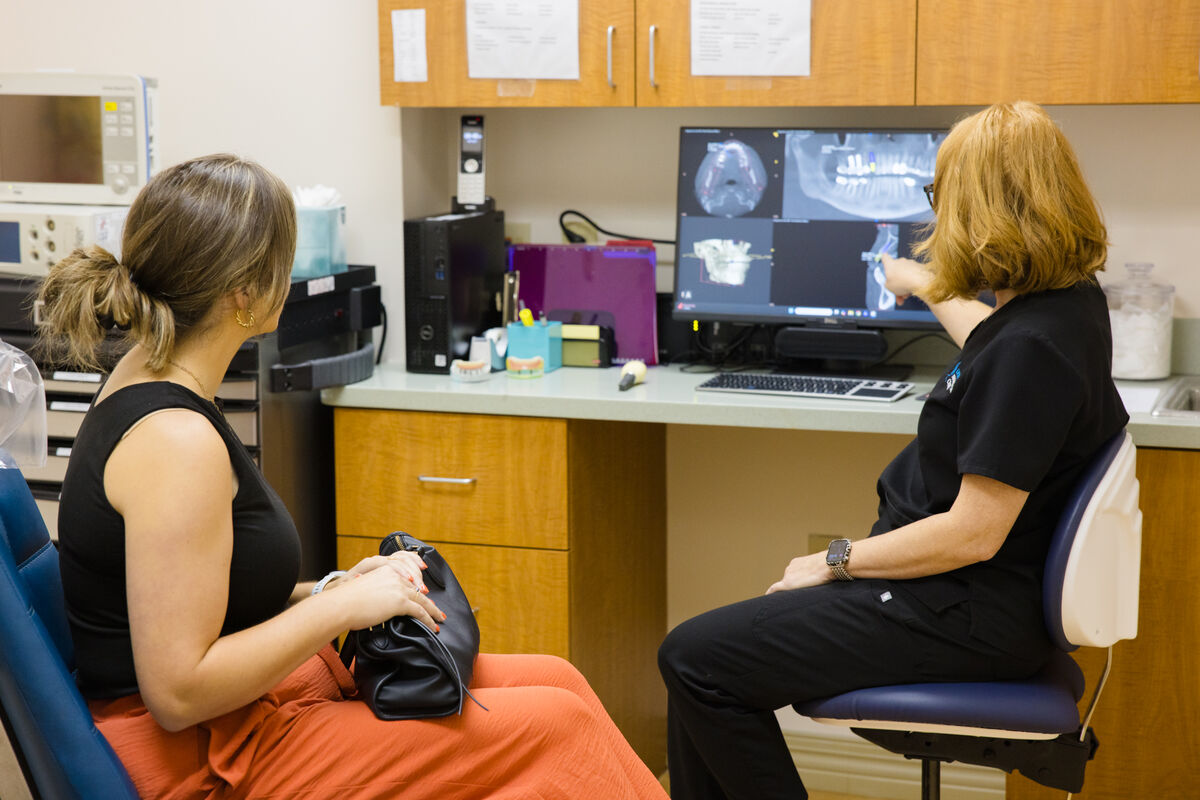 A clinician seated with a patient at a monitor, going through a panoramic dental X-ray together.