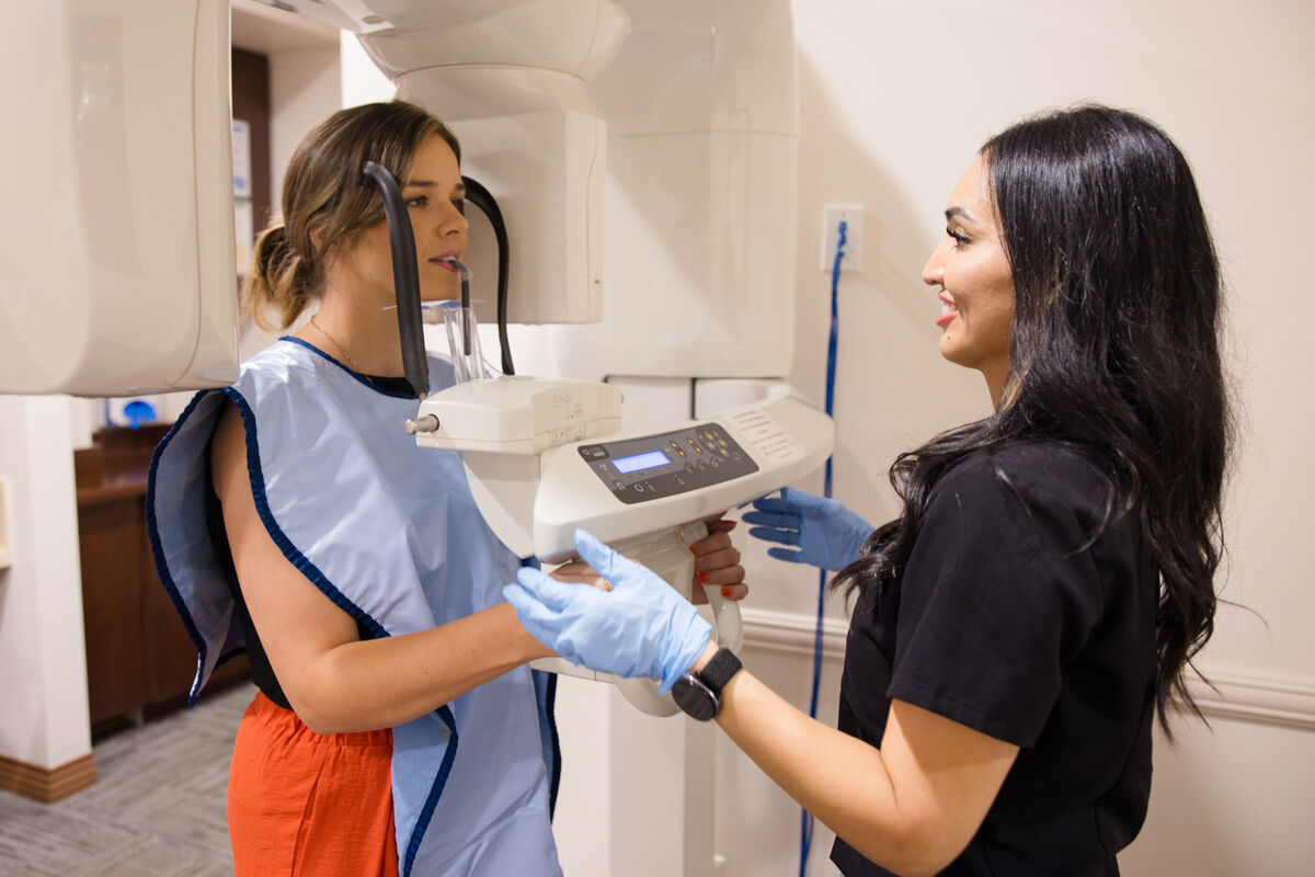A patient standing at a panoramic dental X-ray machine while a team member operates the control panel beside her.