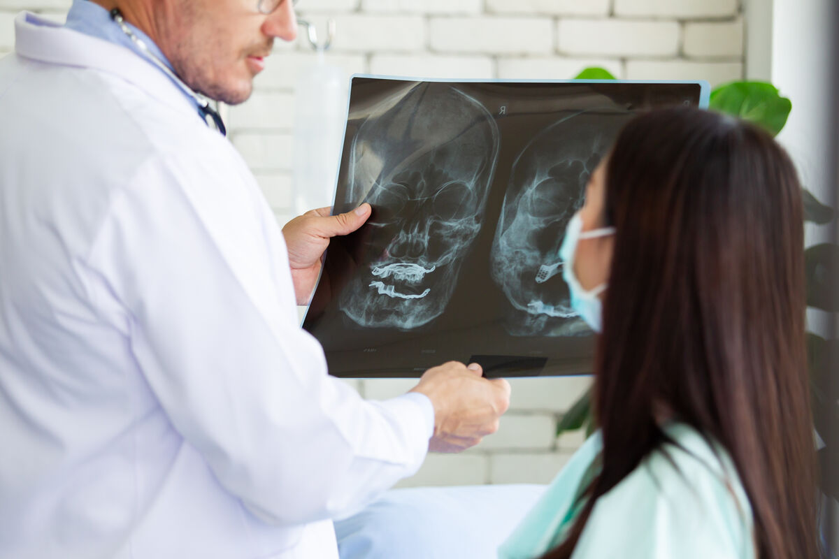 A clinician reviewing skull X-rays on a lightbox with a patient seated beside him.