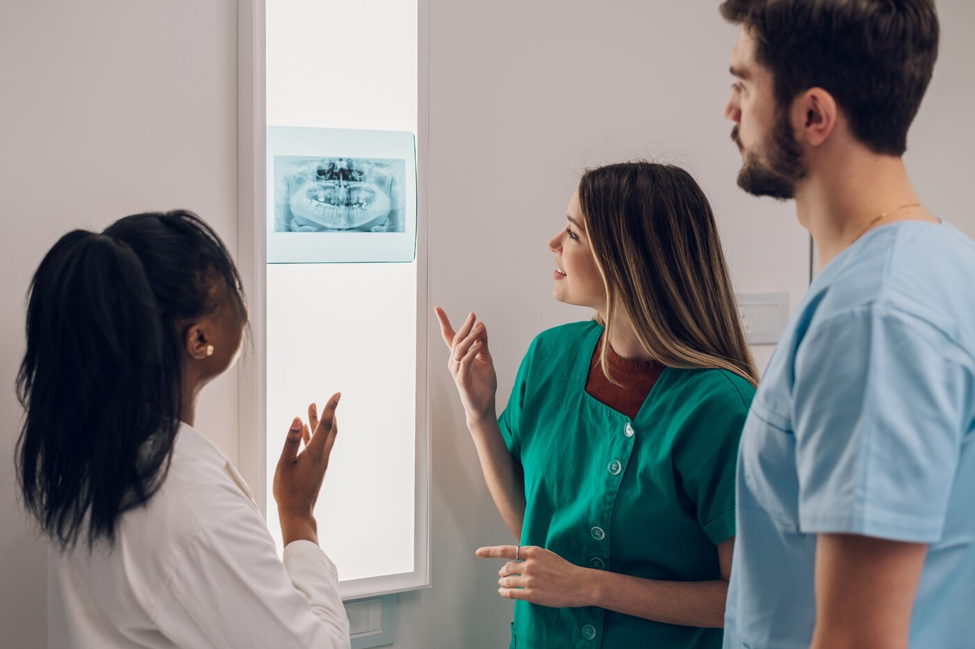 Three clinicians studying a jaw X-ray together on a lightbox while discussing a case.