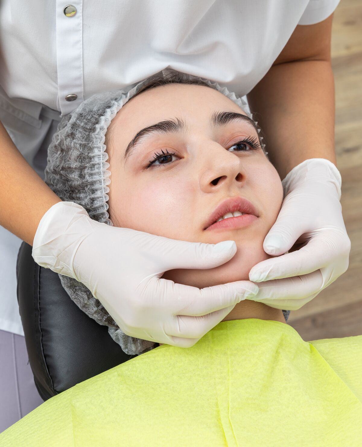 A clinician's gloved hands examining the jaw alignment of a patient reclined in the chair.