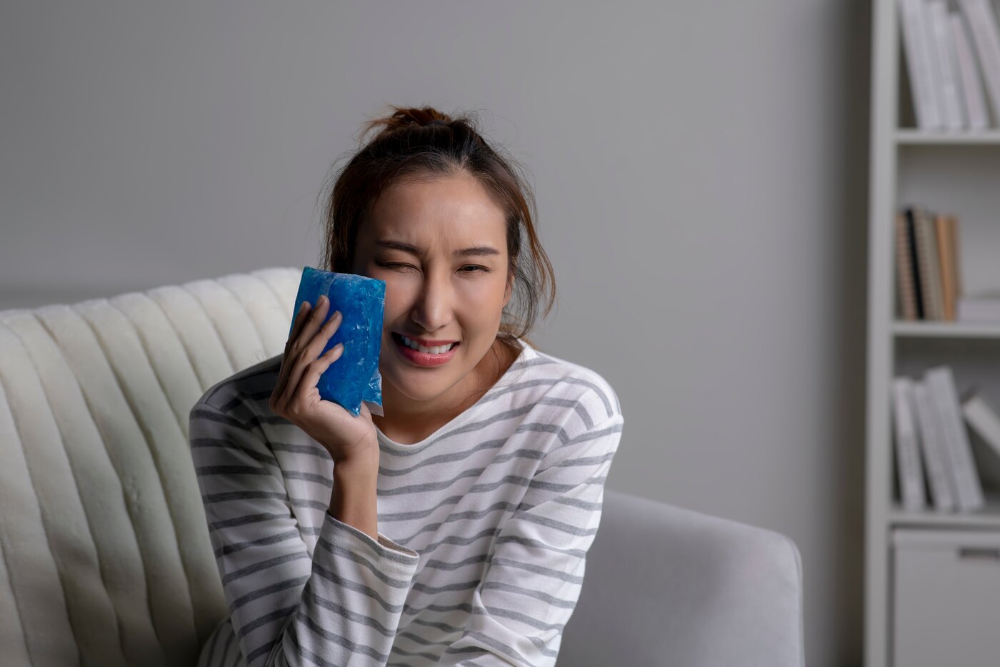 A woman resting at home with a cold pack held against her cheek to ease post-operative swelling.