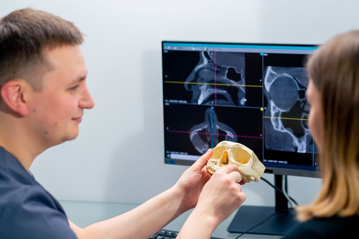 A clinician and a patient reviewing three-dimensional facial scans on screen while he holds a jaw model.