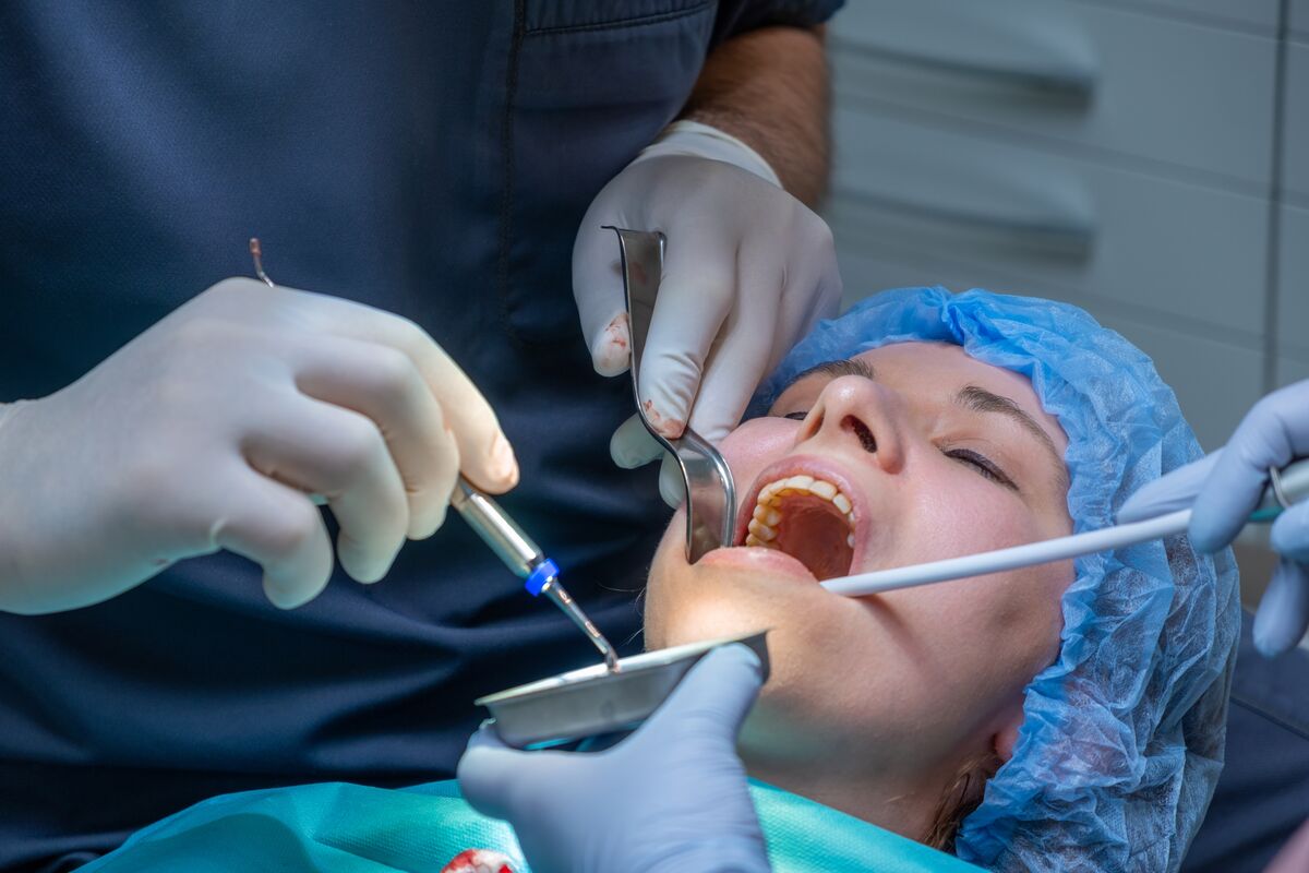 An oral surgery in progress: a patient in a surgical cap with retractors and suction in place while gloved hands work.